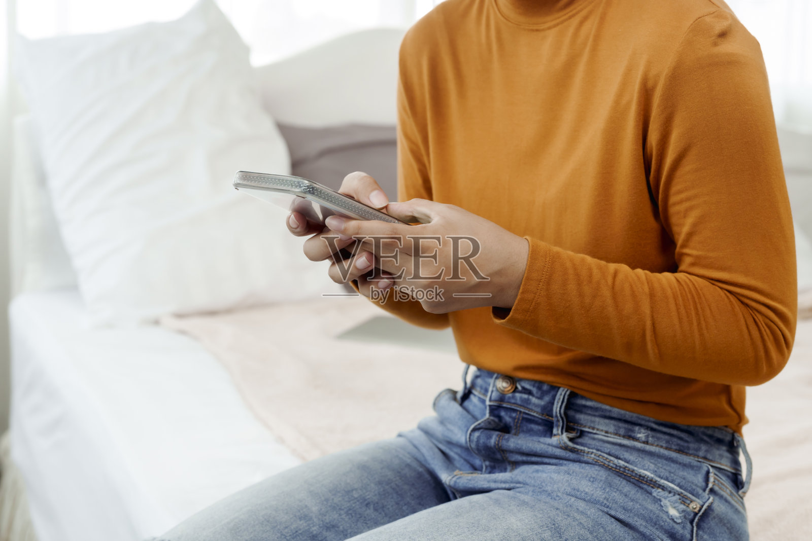 亚洲妇女，黄色衬衫，长发，他拿着电话，按在卧室的床上。照片摄影图片