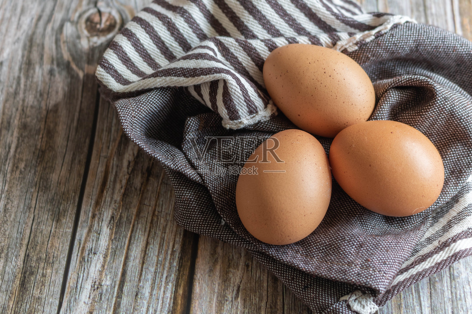 棕色的鸡蛋放在铺着棕色布料的木地板上。照片摄影图片