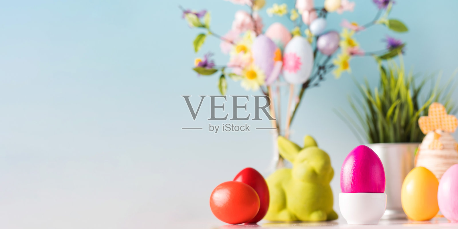 复活节的旗帜，彩色的鸡蛋和绿色的兔子在蓝色的背景和一个花枝。本空间照片摄影图片