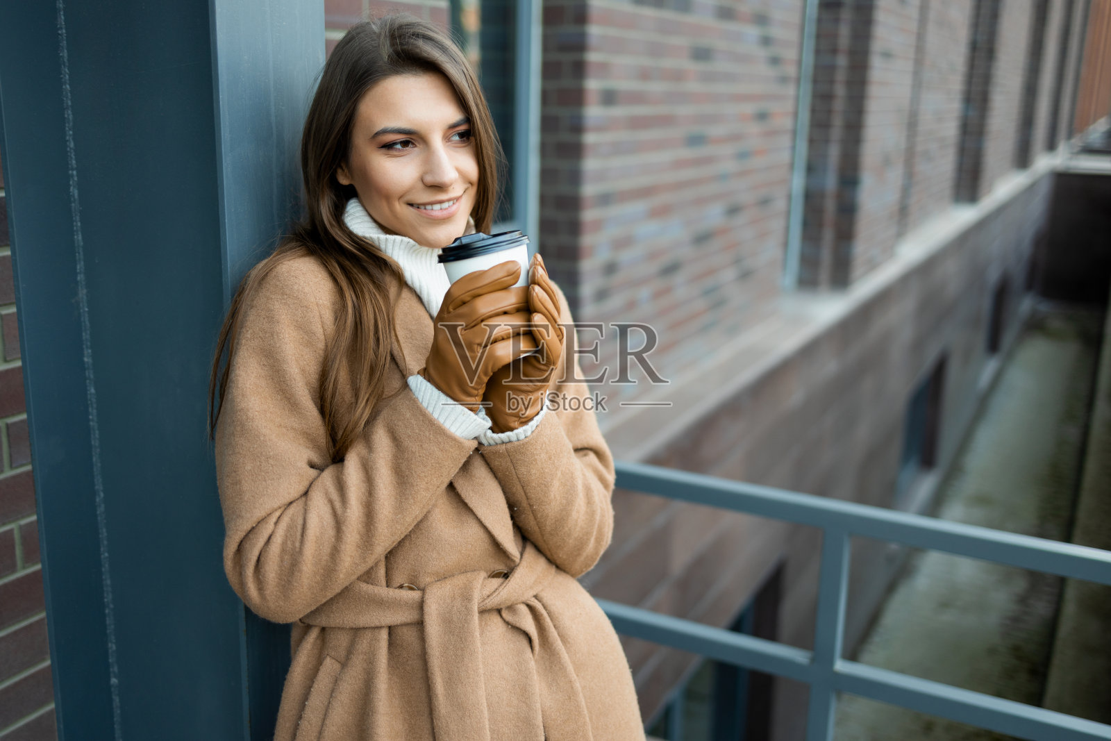 一个美丽的年轻女子的肖像，她的手拿一杯热咖啡在户外照片摄影图片