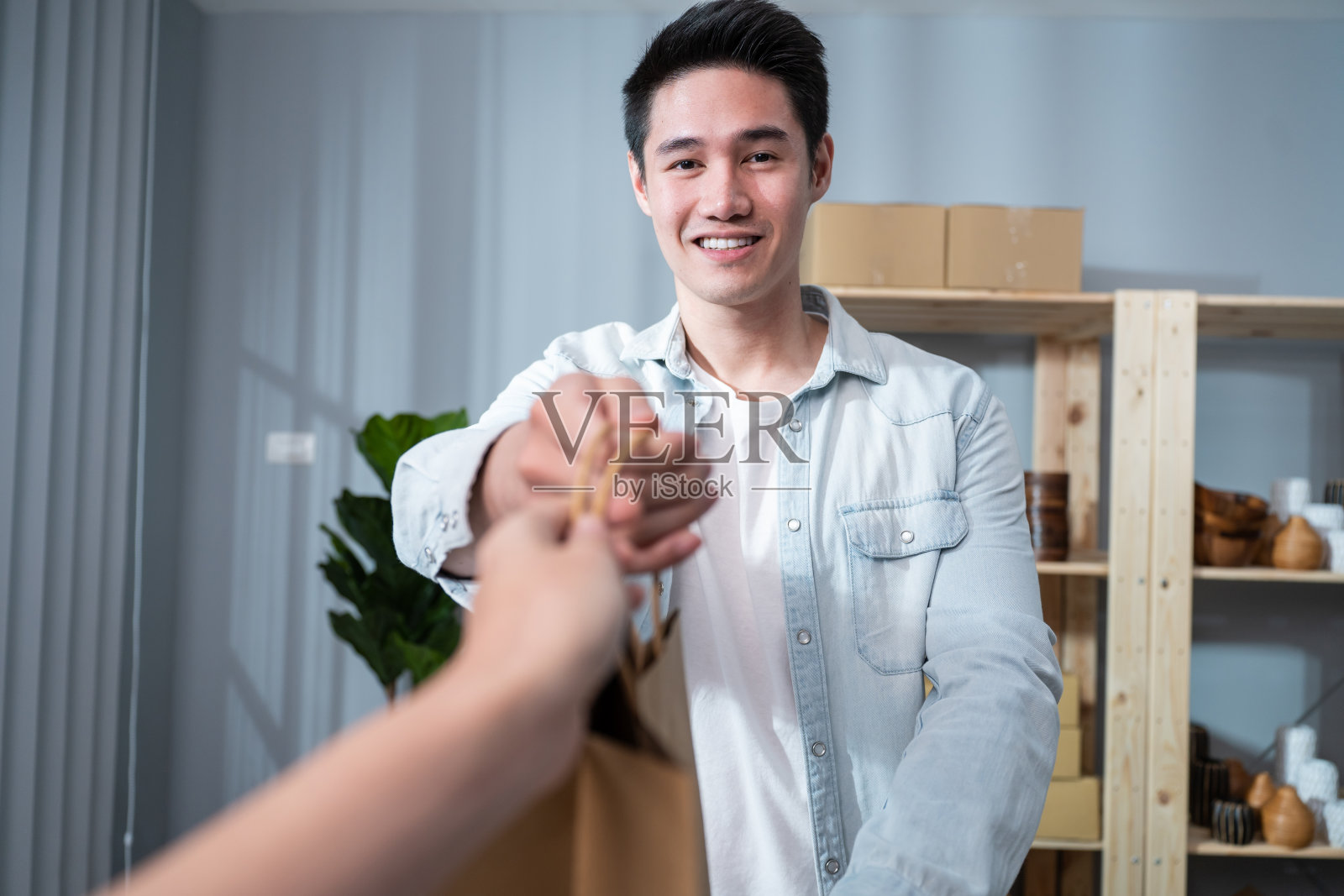 亚洲年轻商人向客户处理产品订单的肖像。有吸引力的帅哥派送男性微笑，并将购物袋送到女性手中，供托运网上零售到家中商店销售。照片摄影图片