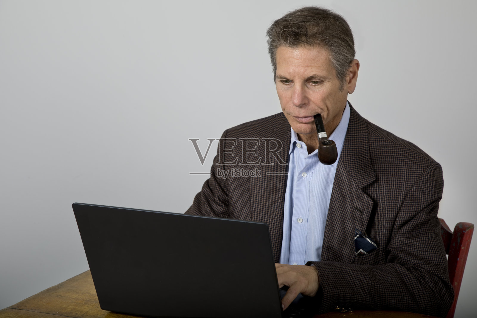 穿着运动夹克的男人抽着烟斗在笔记本电脑前工作照片摄影图片