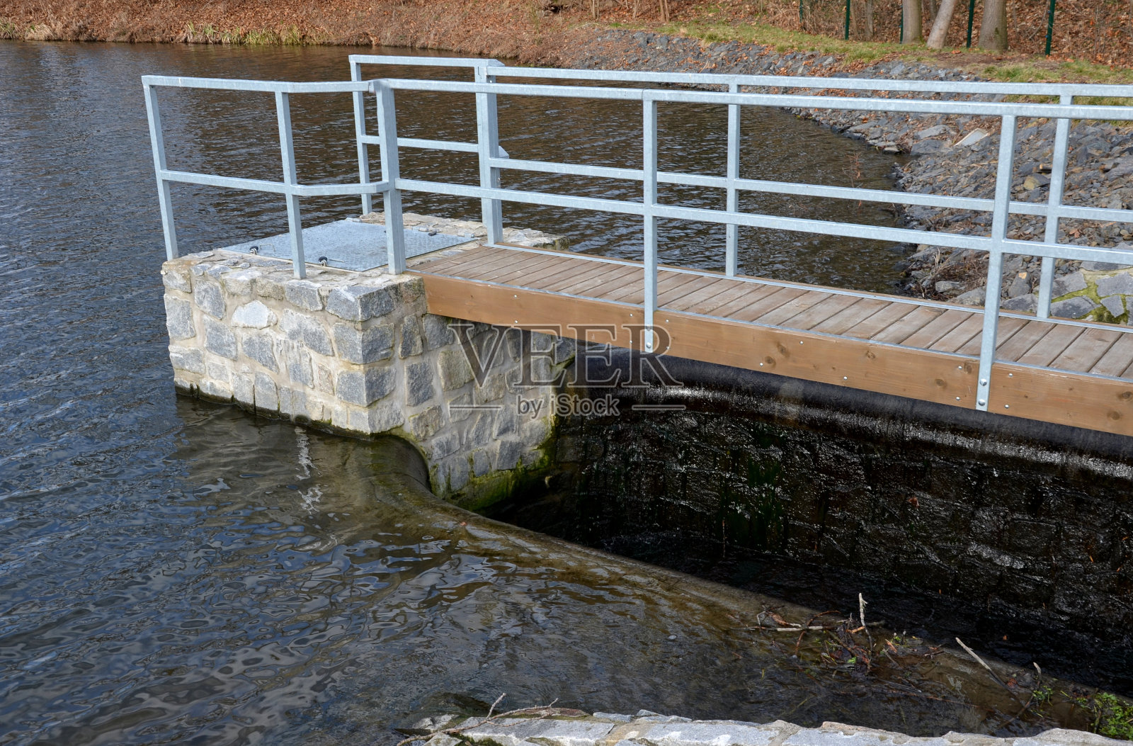 横跨大坝安全溢洪道的桥梁。石桥用天然的灰色平石铺装。在挡土墙的边缘是一个微妙的彩色锻铁栏杆。水从下面流过照片摄影图片