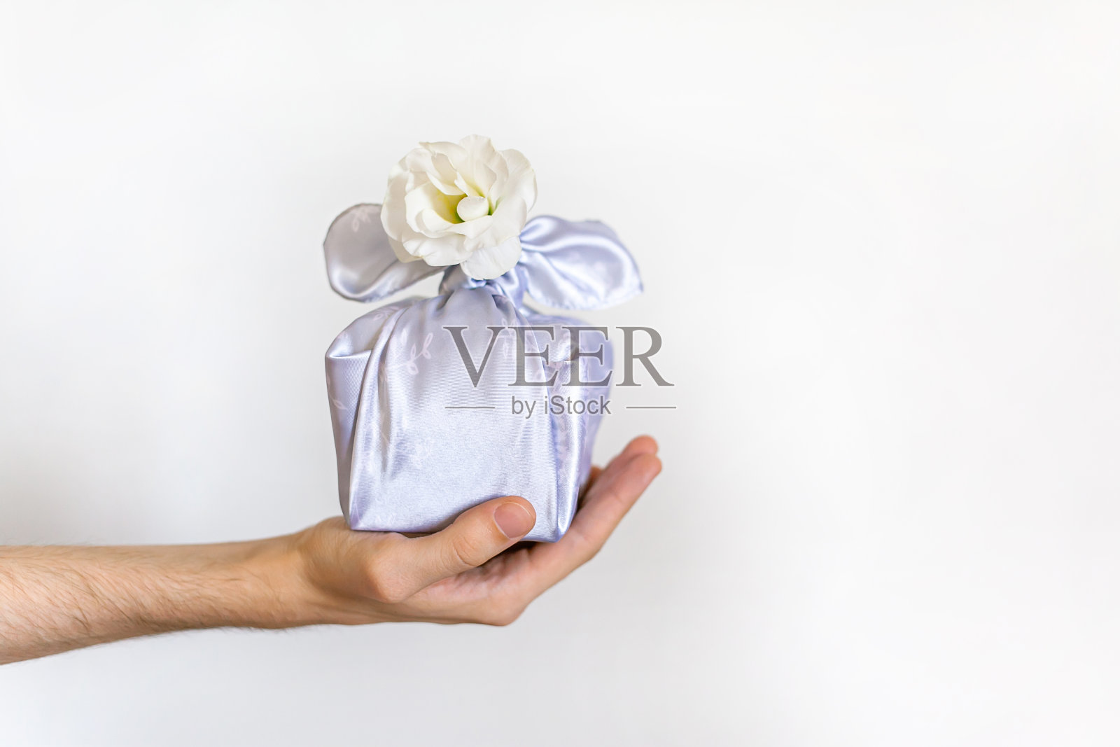 年轻人手拿着用真丝织物包裹的礼盒，用紫檀白花的工艺制作而成。照片摄影图片