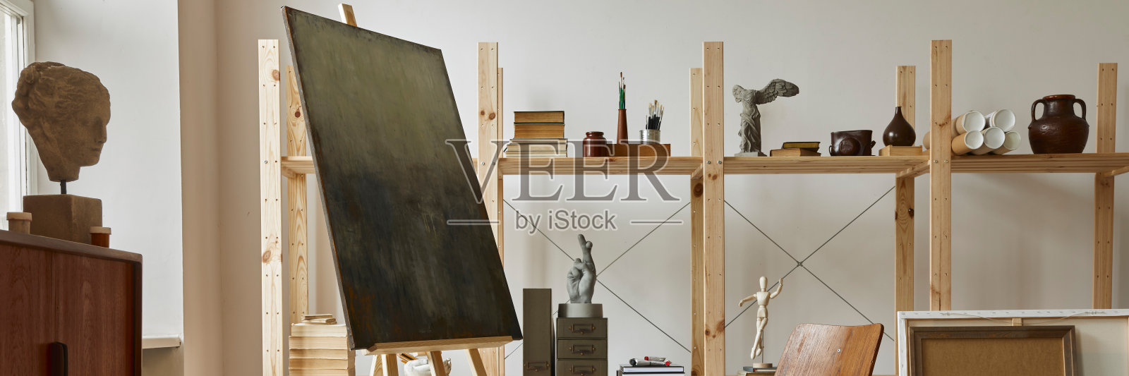 独特的艺术家工作空间与时尚的柚木马桶，木制画架，书柜，艺术品，绘画配件，装饰和优雅的个人物品。艺术家的现代工作室。模板。照片摄影图片