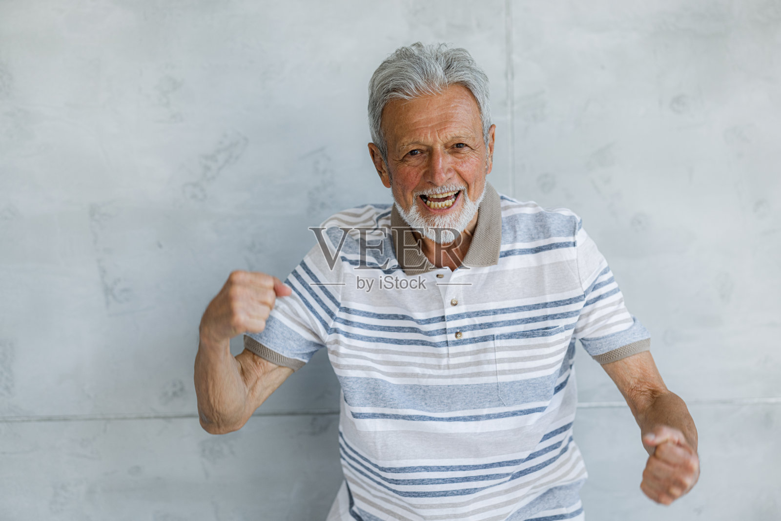 快乐的老家伙靠墙庆祝他的成功。照片摄影图片