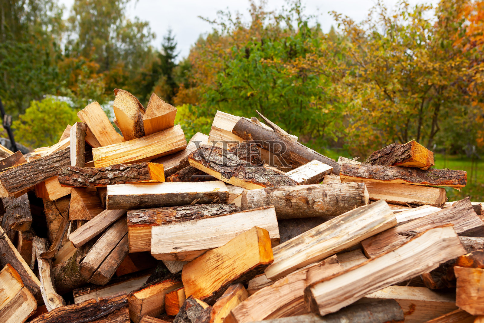 一堆用来给房子供暖的劈柴，在一个开阔的空间里，特写镜头，背景是一个秋天的花园。照片摄影图片
