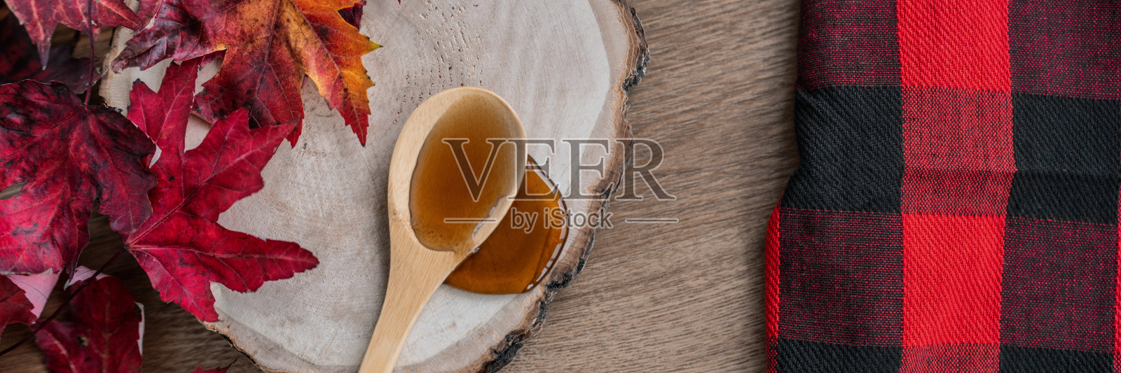 甜枫糖浆甜品配方配料，液体从木勺上滴在原木上乡村糖小屋旗帜全景与水牛格子和红叶照片摄影图片