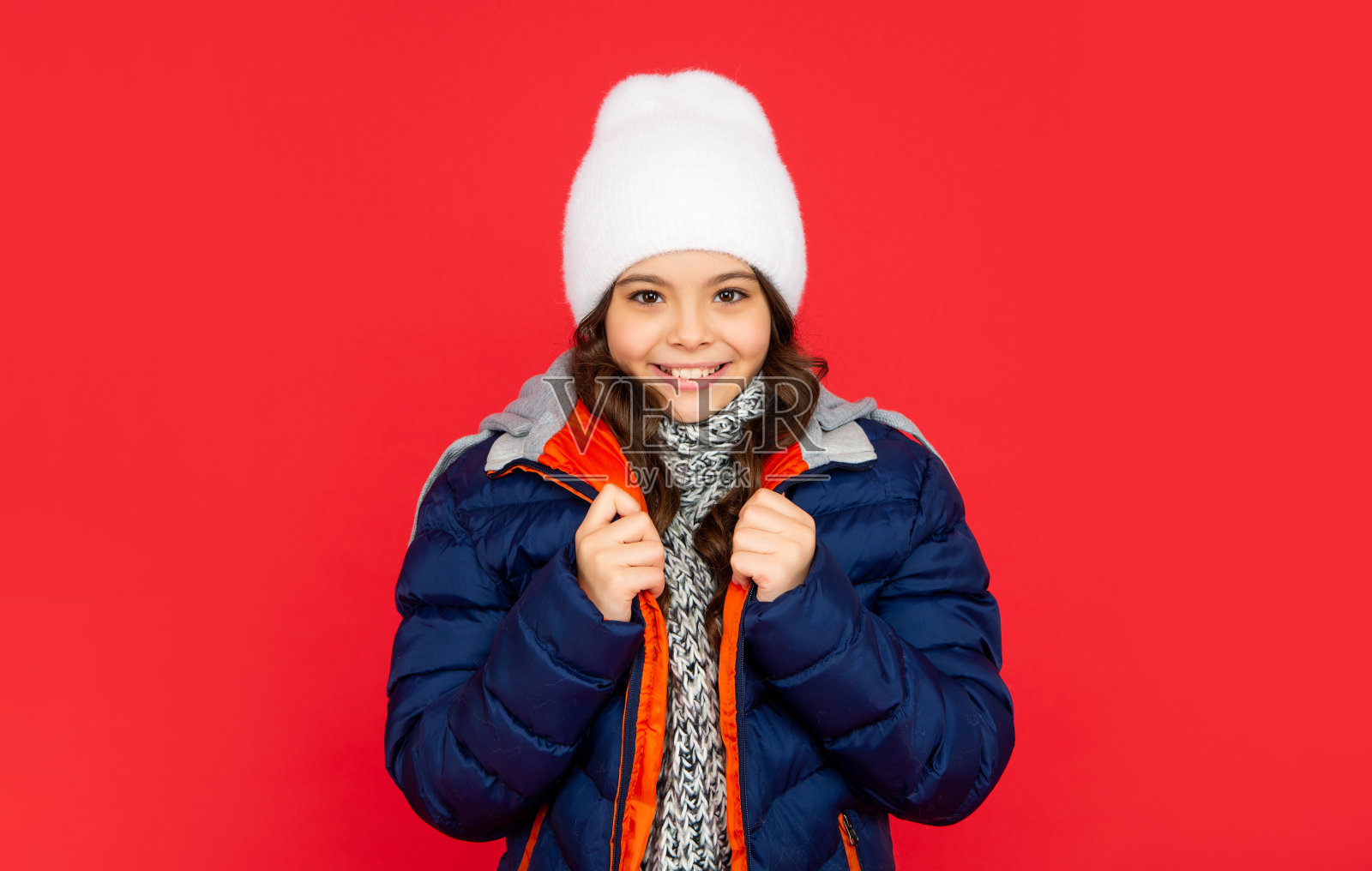 红色背景上的漂亮少女。孩子的肖像，穿着暖和的衣服和围巾。照片摄影图片