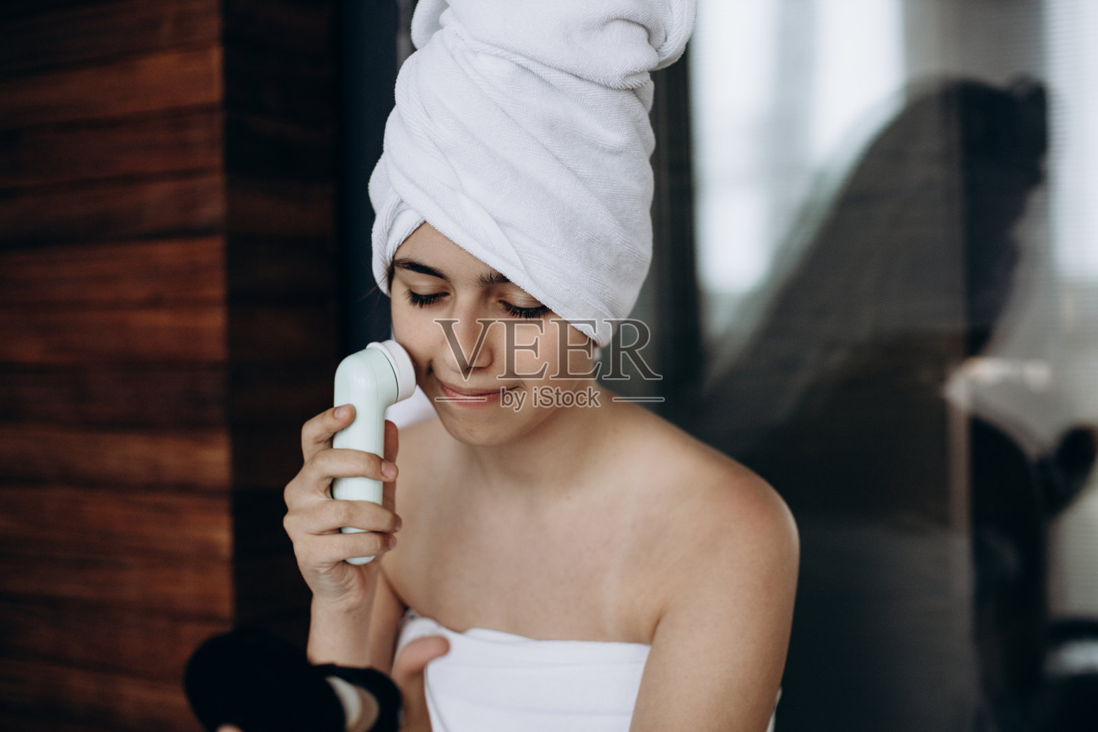 小女孩头戴毛巾，用无线电动按摩器进行面部按摩照片摄影图片