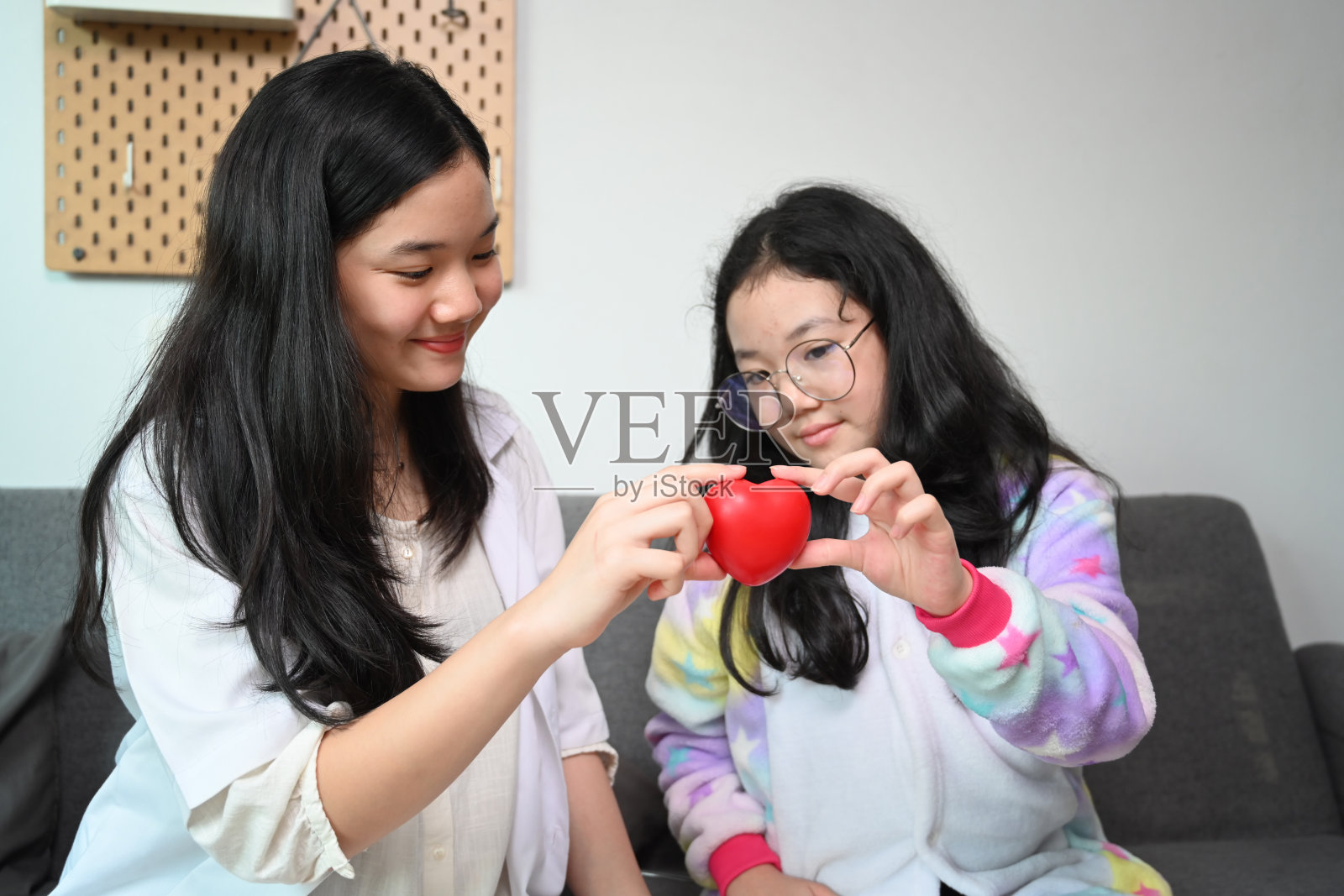 微笑的亚洲女孩穿着医疗制服假装医生与她的妹妹在家里玩。照片摄影图片