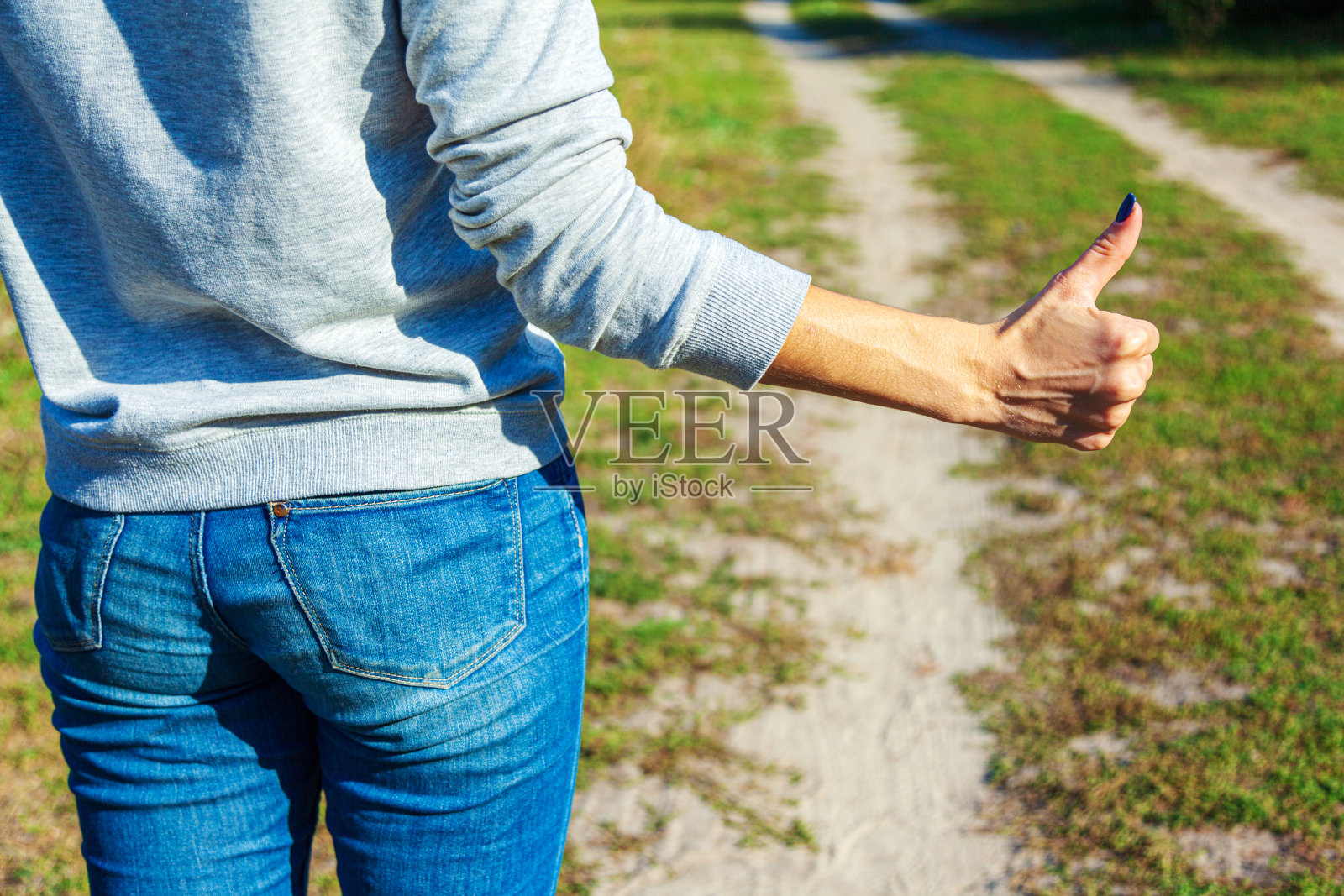 皮肤白皙的女性手竖起大拇指示意搭车。照片摄影图片