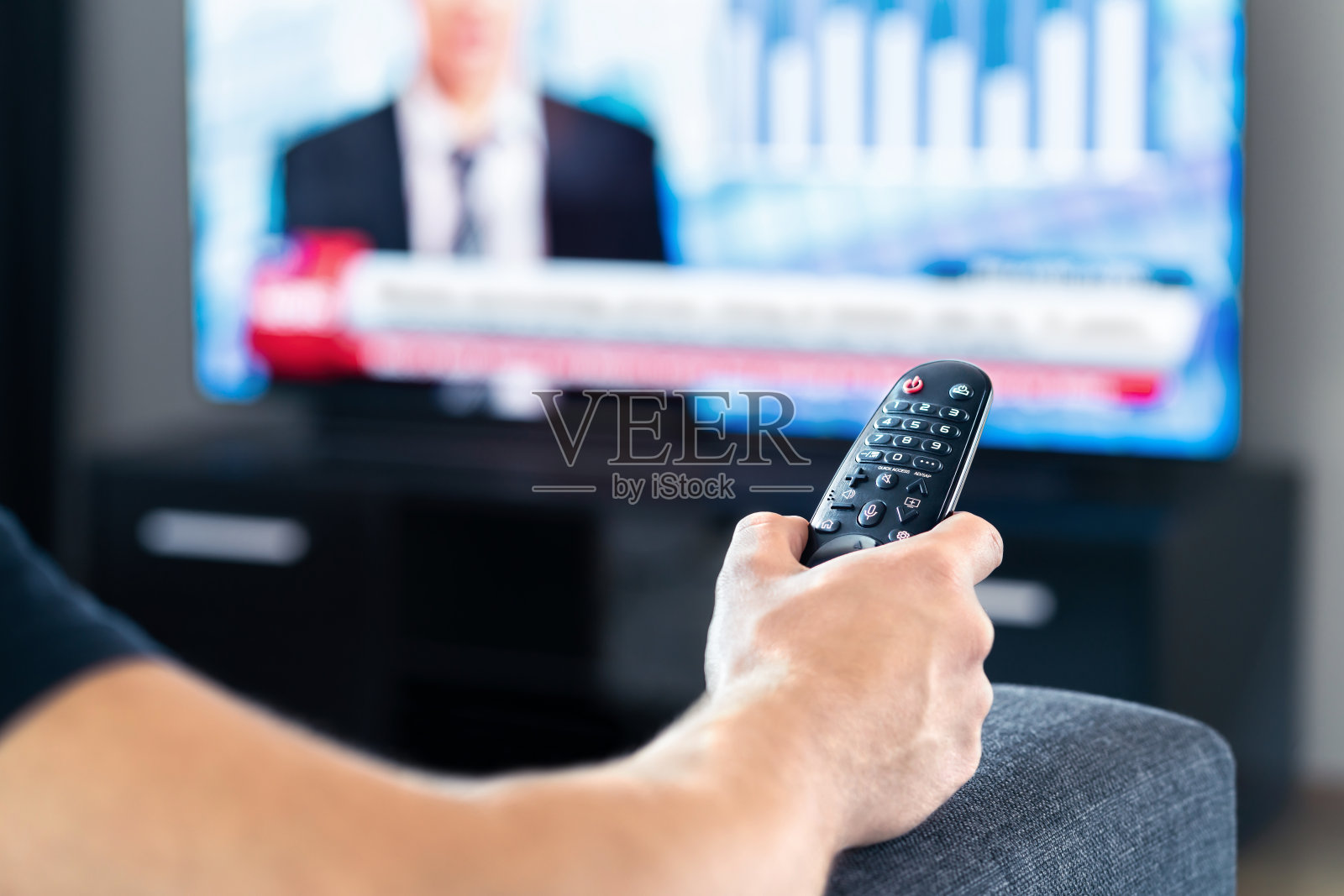 男人坐在家里的沙发上看电视新闻节目。手里拿着电视遥控器。政治、商务或金融网络渠道。在监控屏幕上进行在线直播。照片摄影图片