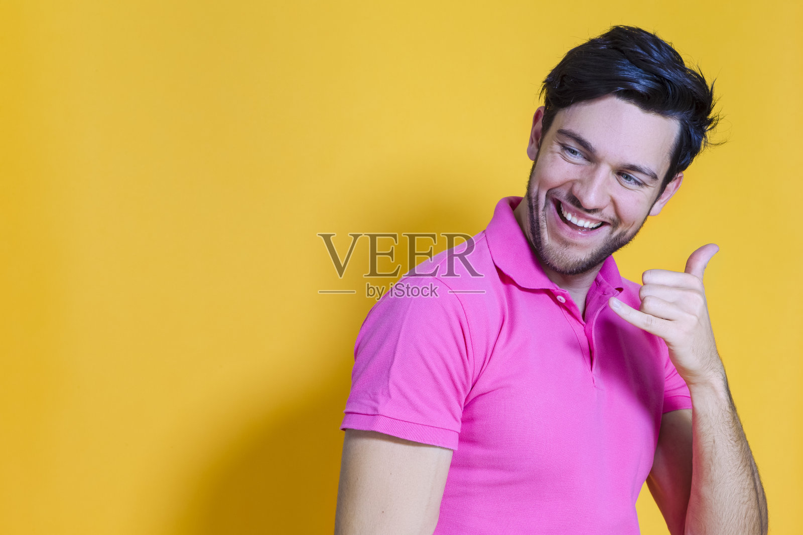 微笑英俊的年轻男子真诚美丽的牙齿微笑与举起的手在黄色背景下，手势手机。照片摄影图片