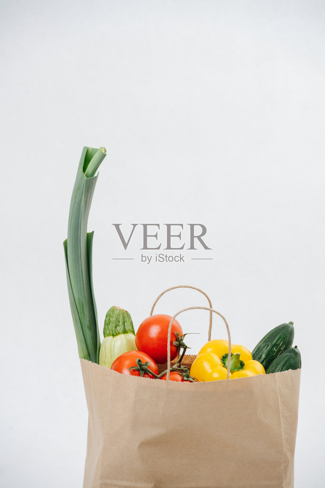 杂货纸袋装满了彩色的蔬菜在白色的背景。照片摄影图片