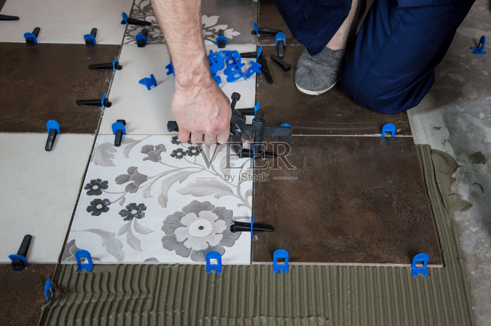 工人把瓷砖放在地板上，用钳子夹住钳子。照片摄影图片