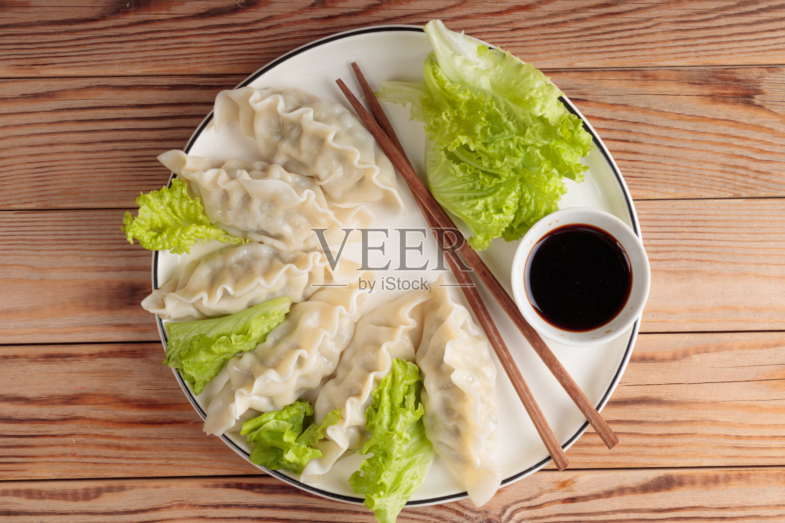 新鲜煮熟的中国饺子，配上酱油和绿色沙拉在木制背景上。照片摄影图片