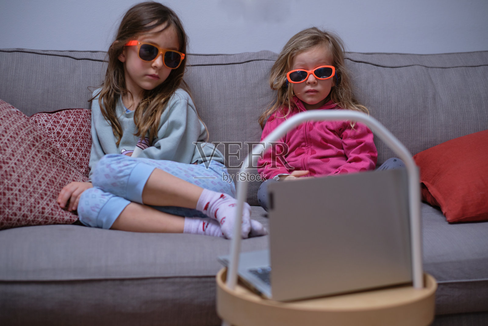 两个小女孩在与Covid有关的家庭住宿期间戴着太阳镜看电视照片摄影图片