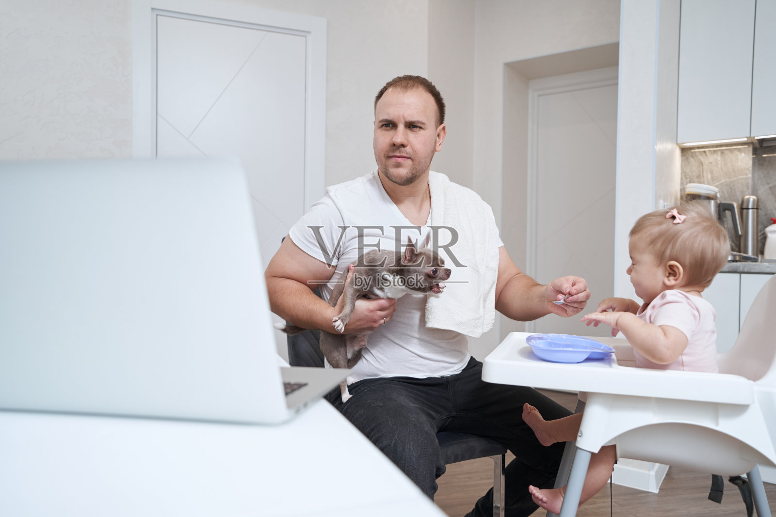 英俊的白人父亲带着宠物在室内高脚椅上给婴儿喂食照片摄影图片