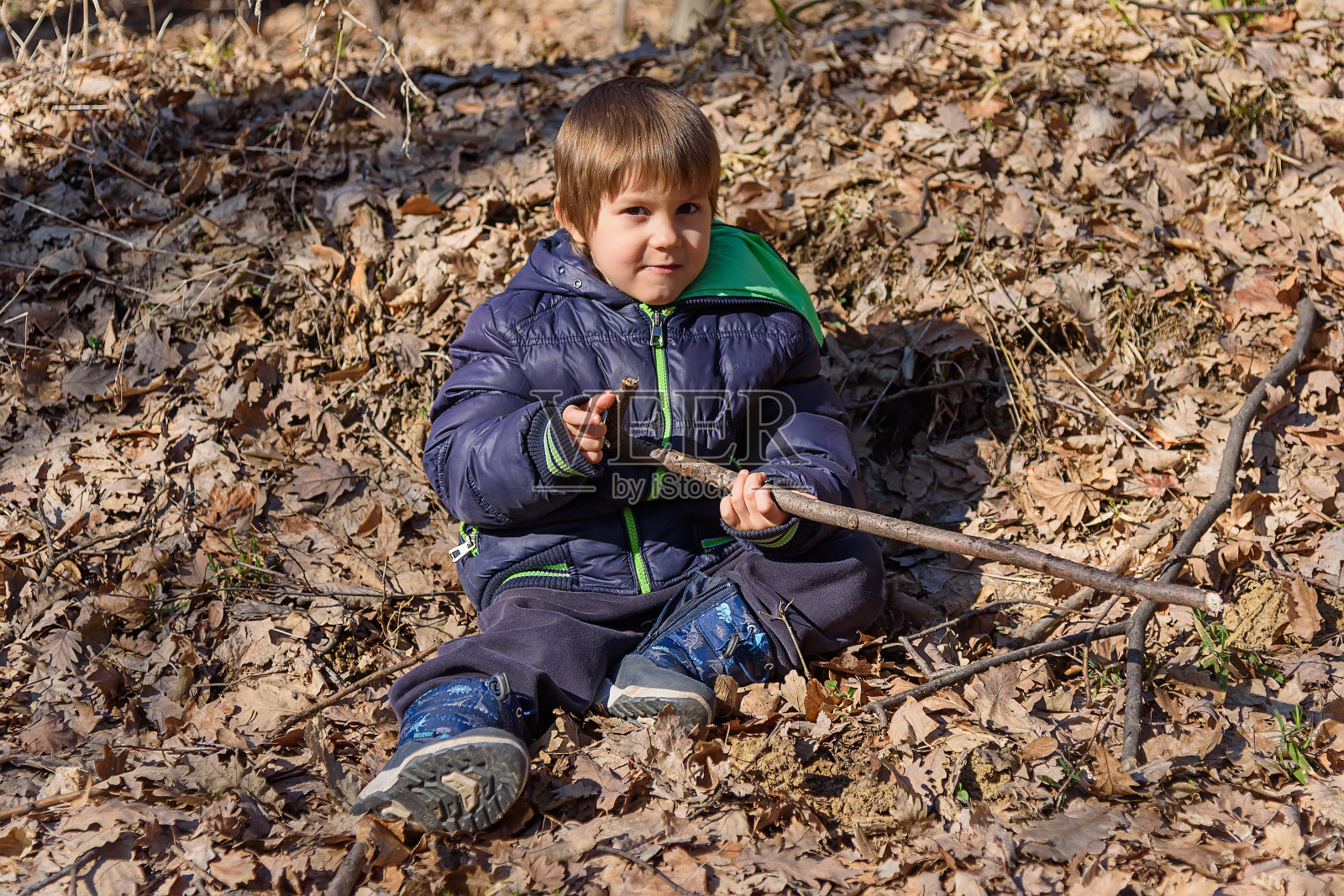 这个男孩躺在树林里的一片叶子上。小男孩带着黄色的秋叶在公园里玩耍照片摄影图片