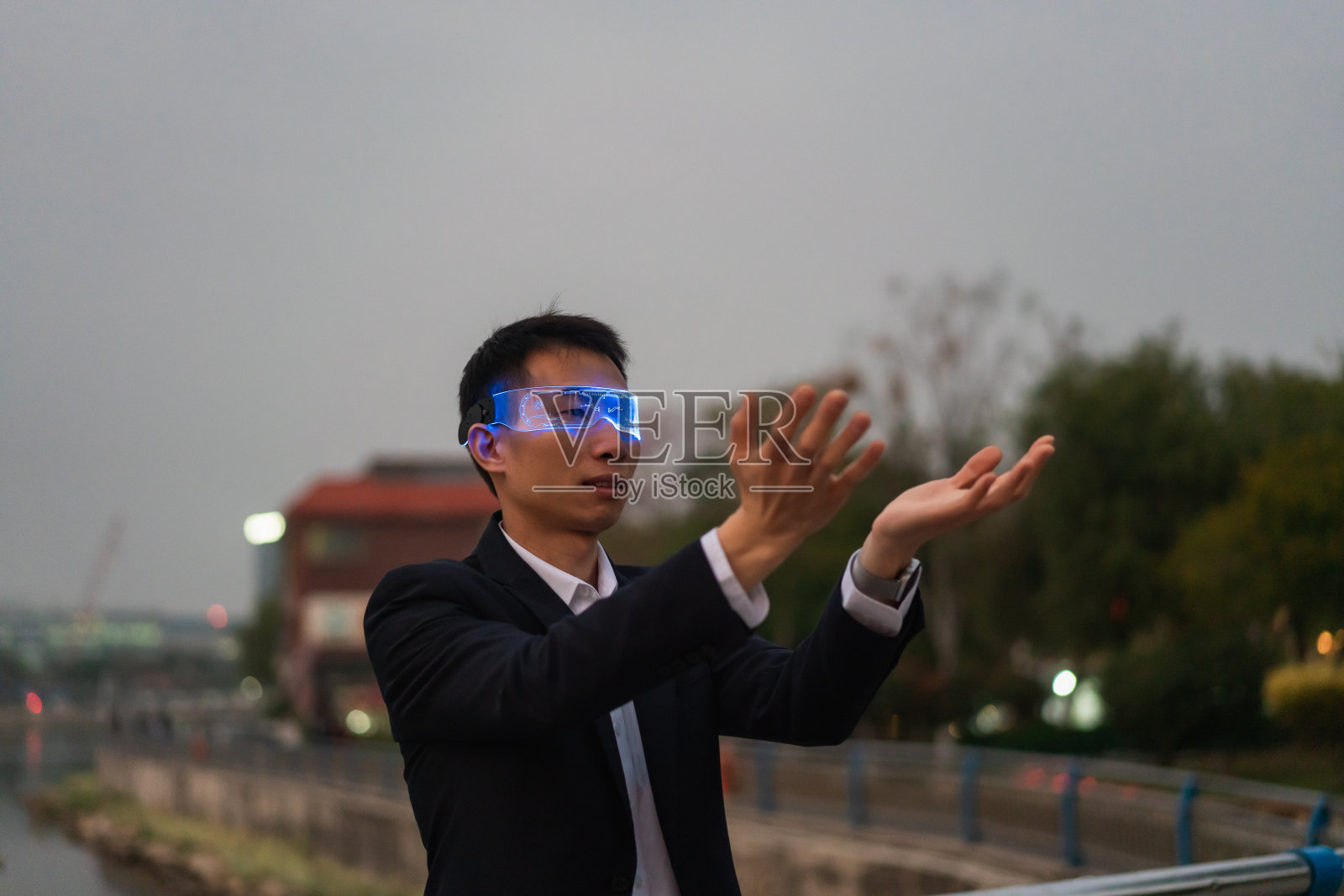 亚洲男性办公室职员在户外使用增强现实眼镜，在夜间体验元宇宙游戏照片摄影图片