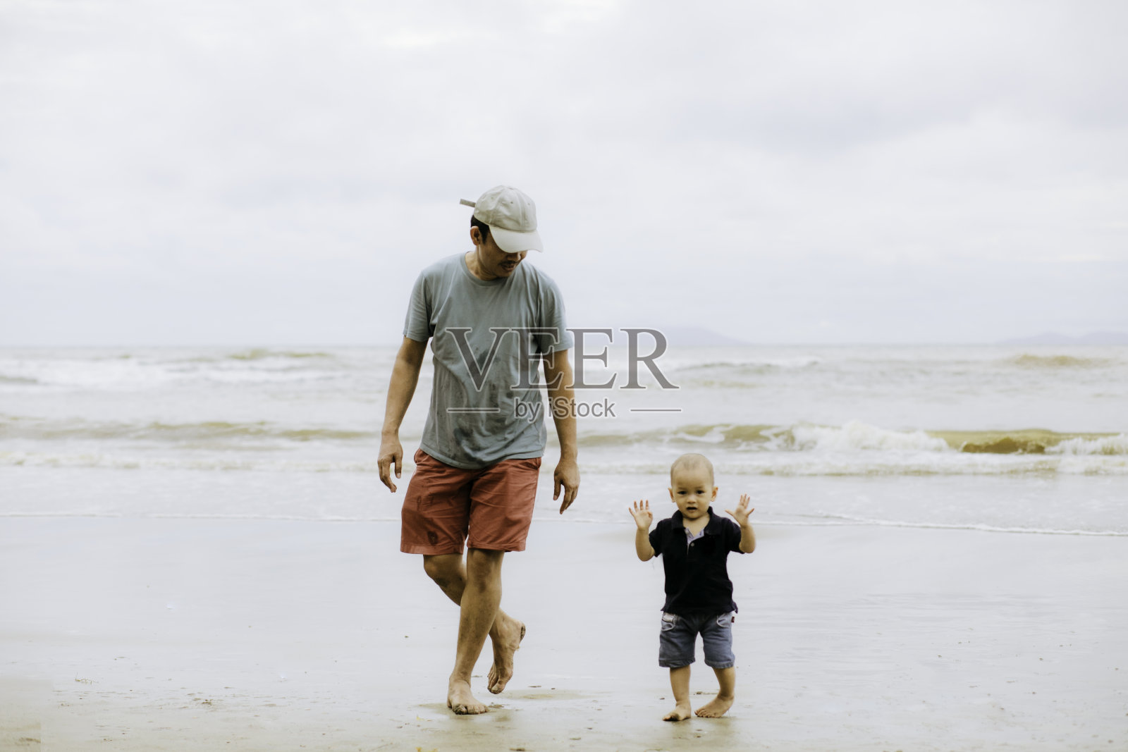 亚洲男人教他的孩子在沙滩上走路照片摄影图片