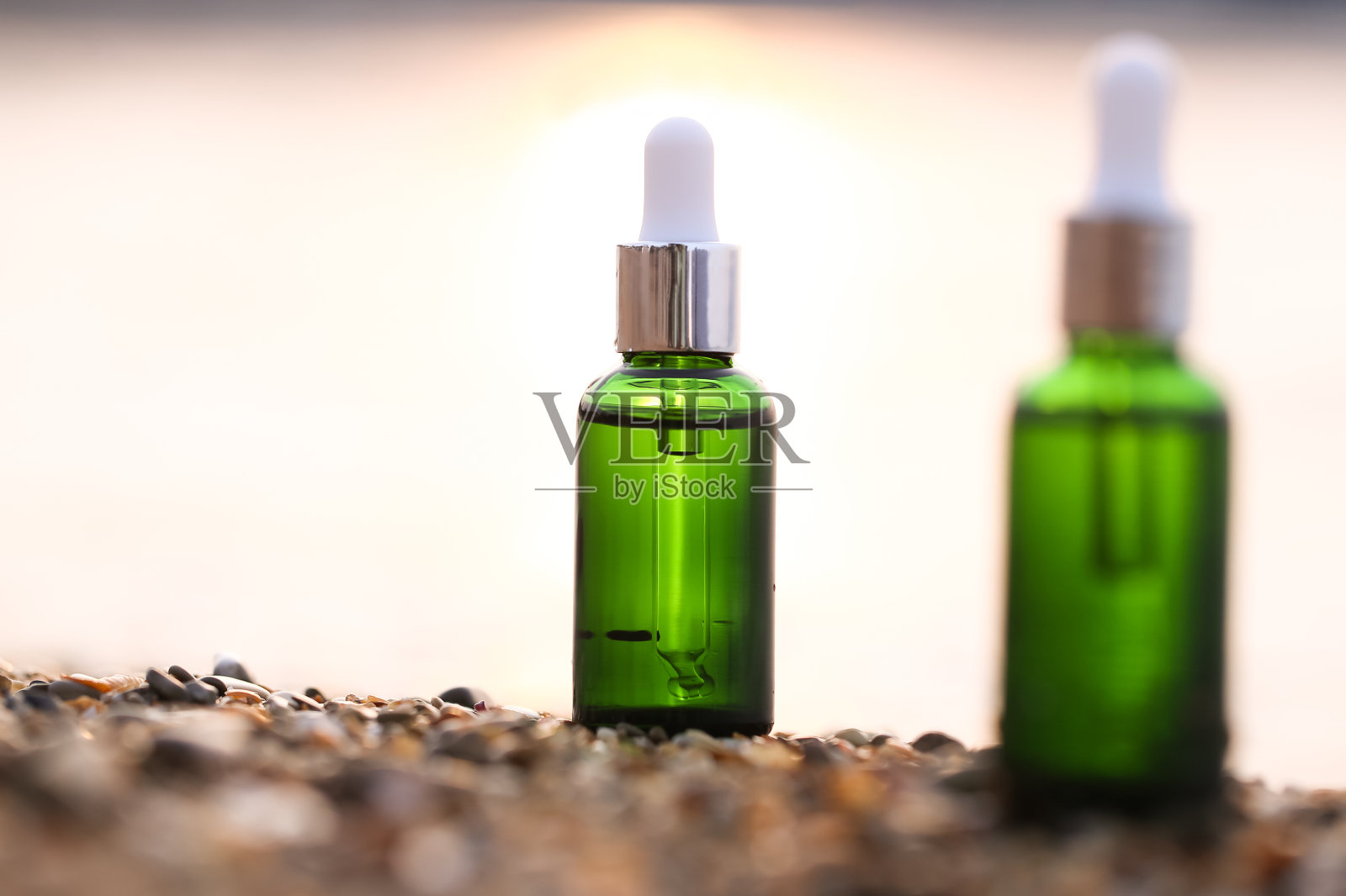 在海边的沙滩上放着一瓶绿色玻璃装的面部精华液照片摄影图片