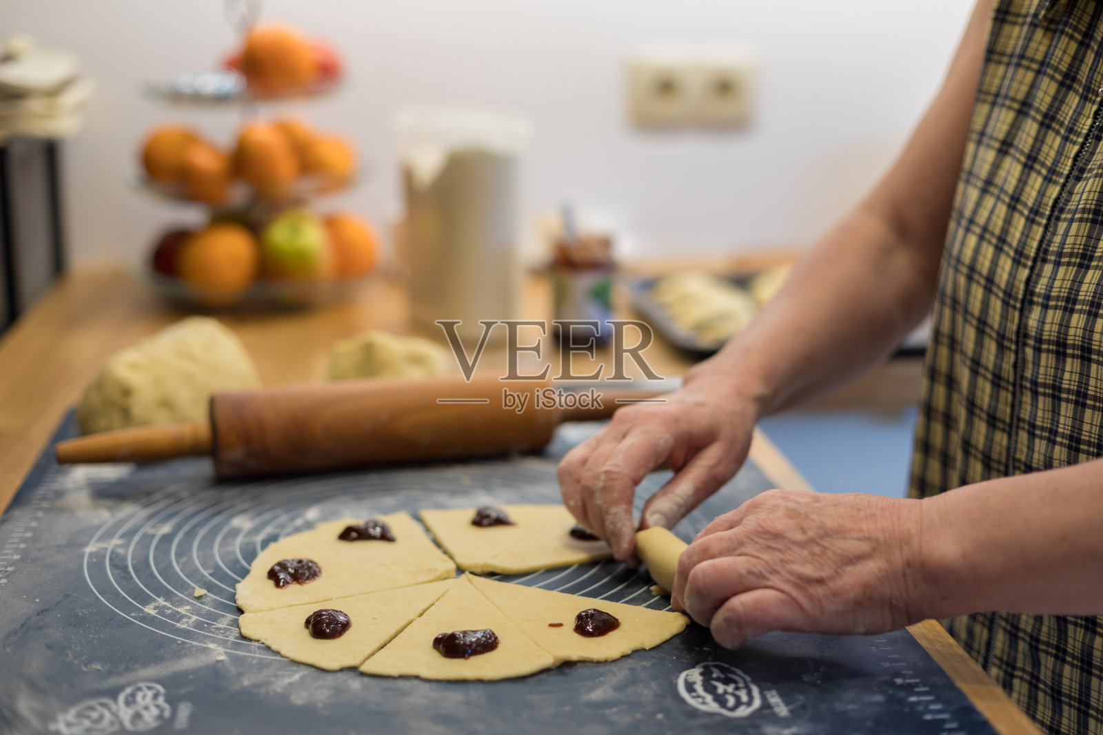 奶奶的手用梅子酱包着自制的羊角面包。照片摄影图片