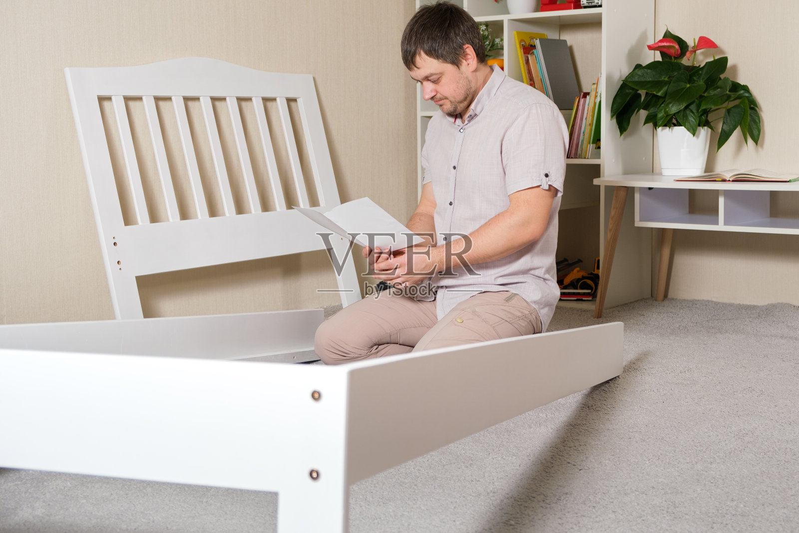 一个困惑的年轻父亲为一个孩子组装床，研究组装家具的说明，他自己的手照片摄影图片