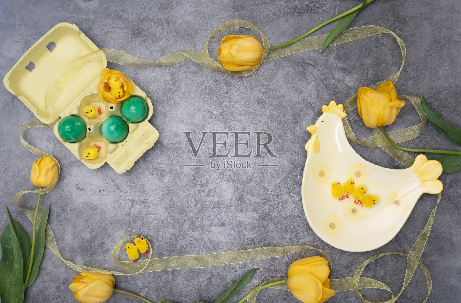 复活节的布置，一盘鸡和黄色的小鸡围绕着绿色的鸡蛋和黄色的郁金香。照片摄影图片