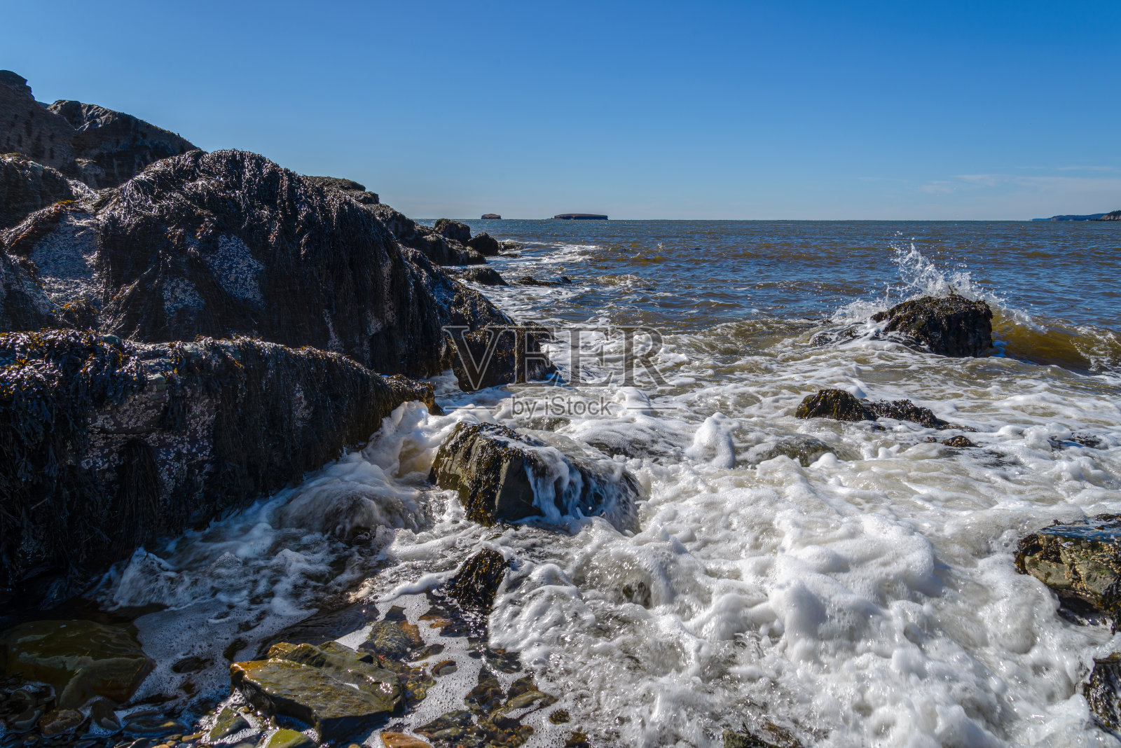 阳光明媚的一天，海浪冲击着岩石海岸照片摄影图片