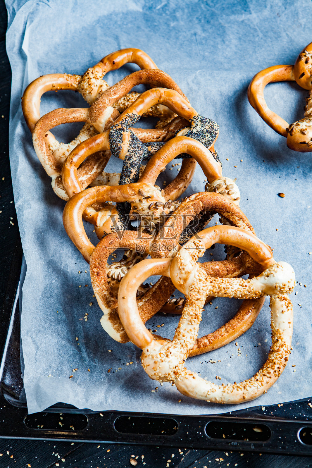 新鲜自制软椒盐卷饼。黑色背景上不同类型的带籽烤百吉饼。照片摄影图片