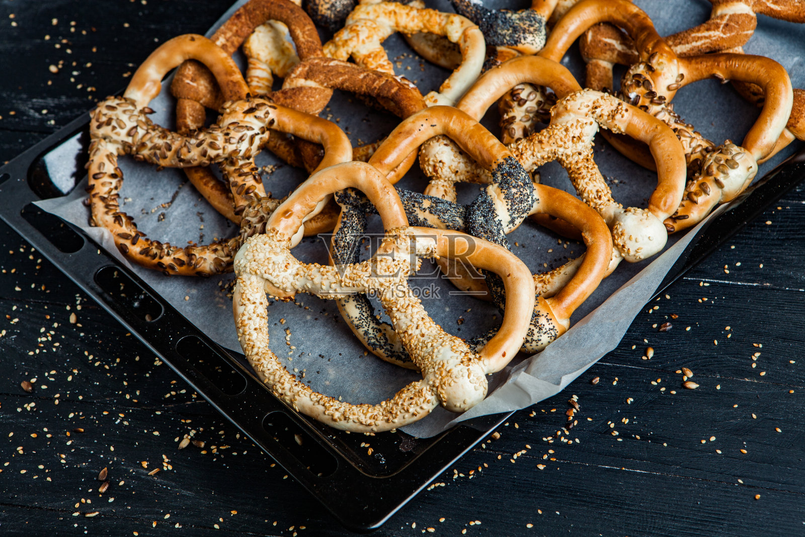 新鲜自制软椒盐卷饼。黑色背景上不同类型的带籽烤百吉饼。照片摄影图片