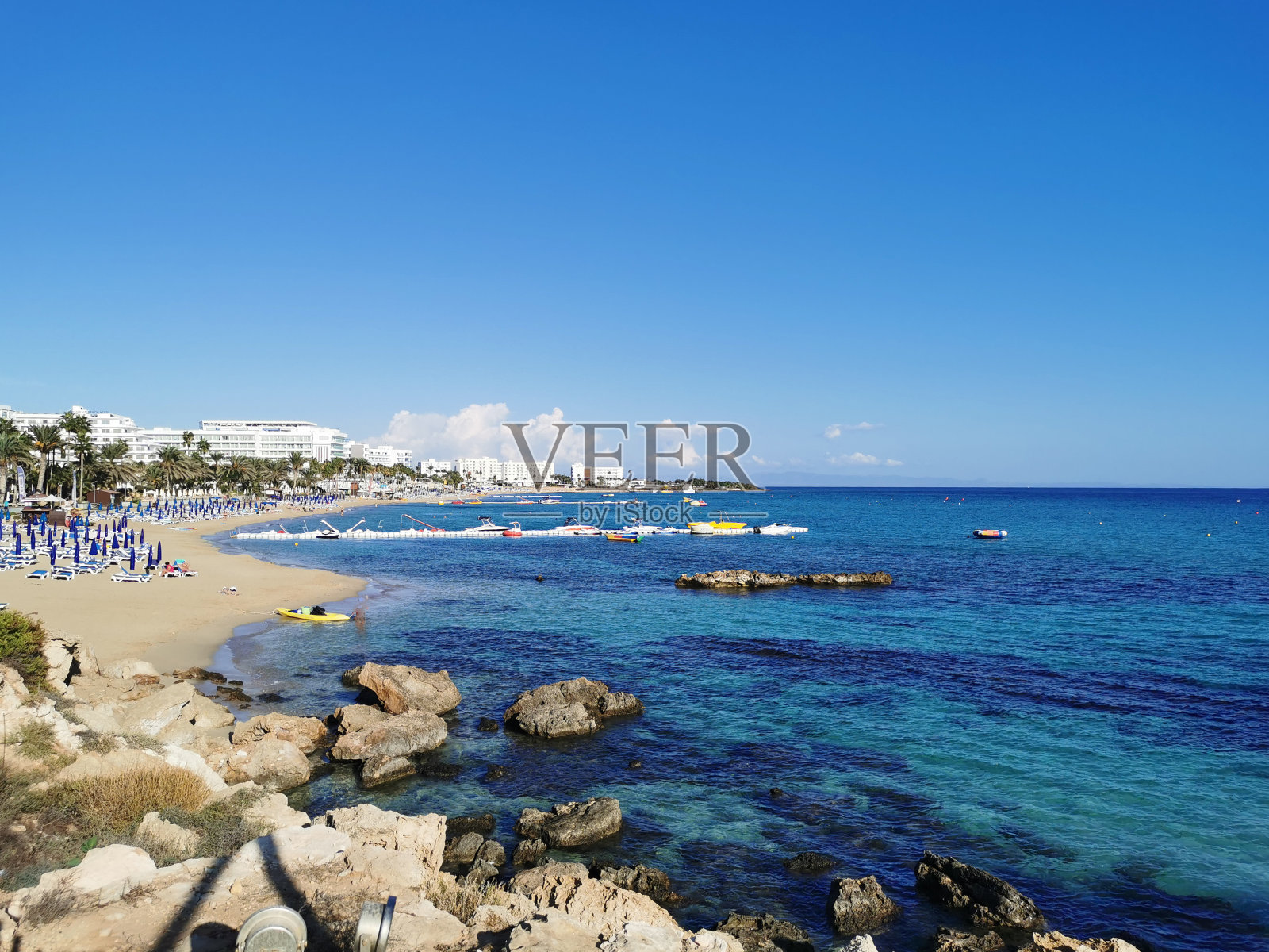 海岸附近的巨石，地中海清澈的海水，在蓝天白云的背景下，可以看到巨大的日出沙滩和酒店。照片摄影图片