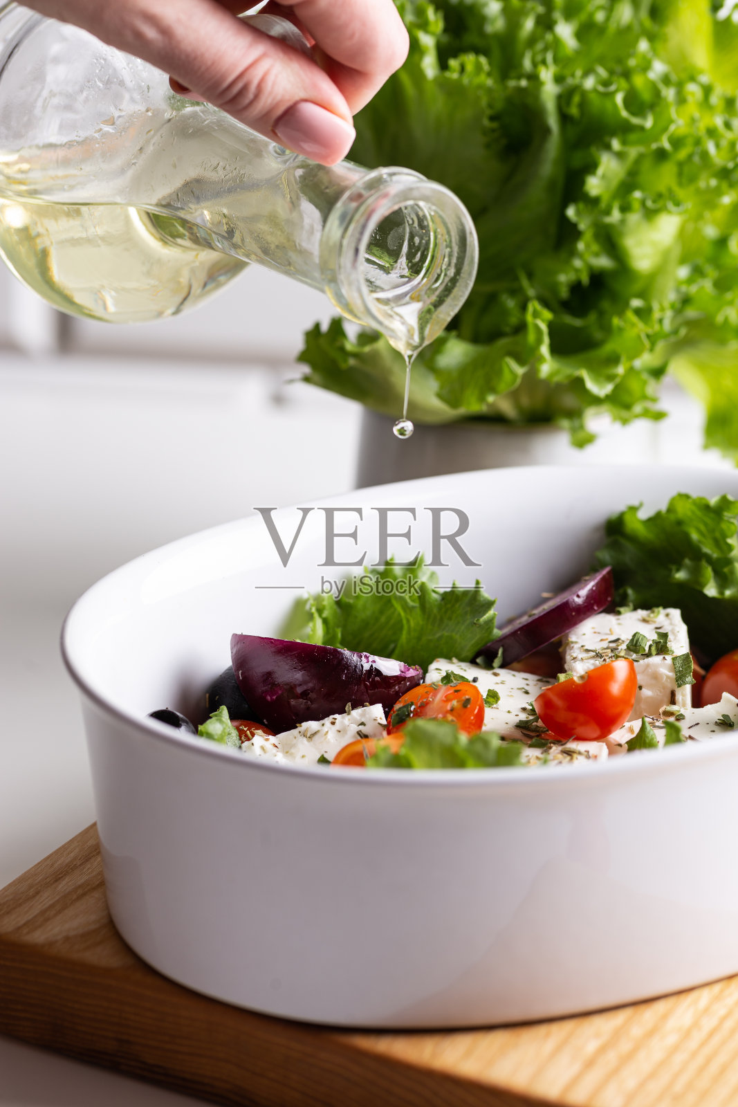 一个女人正在往一碗希腊沙拉里倒橄榄油照片摄影图片