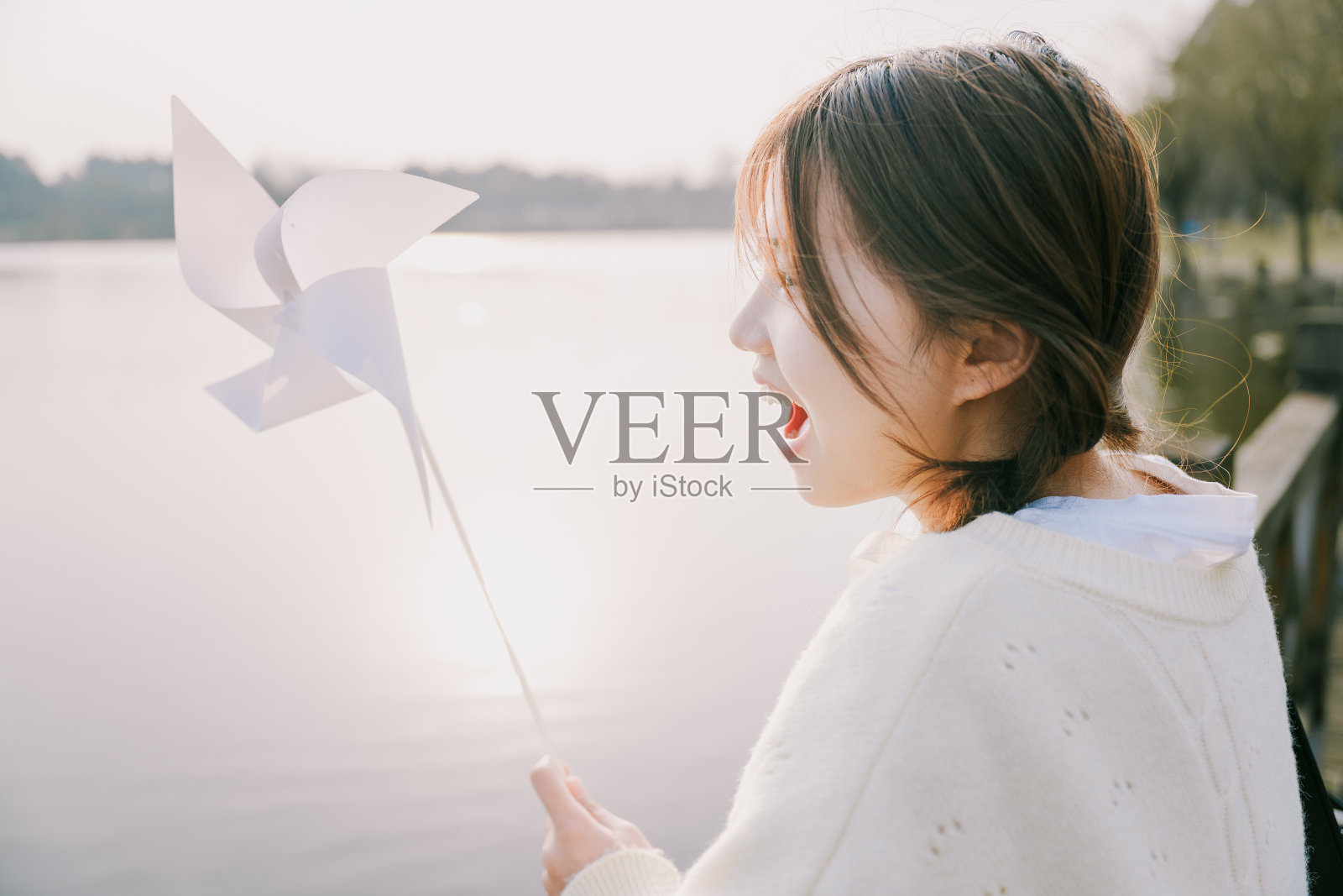 一个美丽的亚洲女孩与纸风车笑在湖在黄昏照片摄影图片