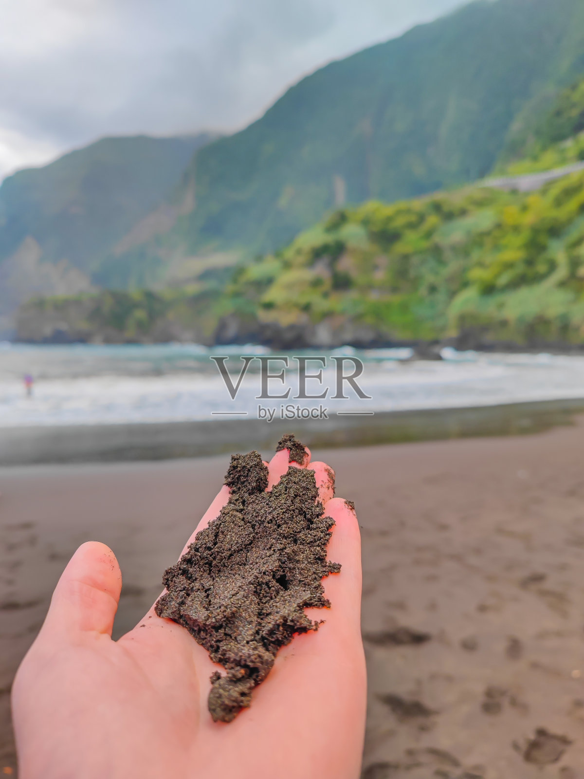 在马德拉岛的Seixal海滩，一名男子手里拿着黑色的沙子照片摄影图片
