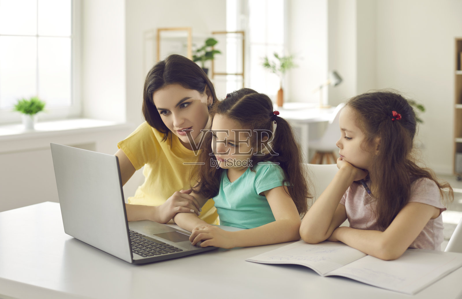年轻的白人母亲带着两个小女儿用笔记本电脑做作业照片摄影图片