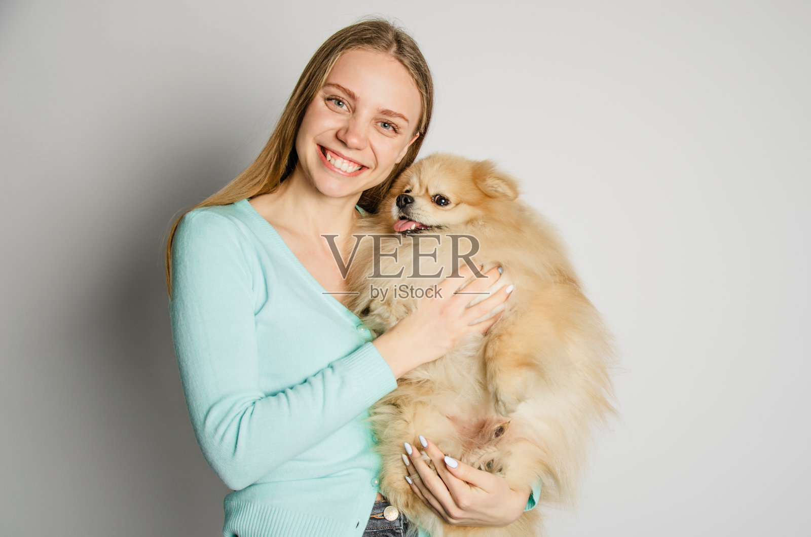 一个金发女孩抱着一只博美犬，看着镜头。肖像照片摄影图片