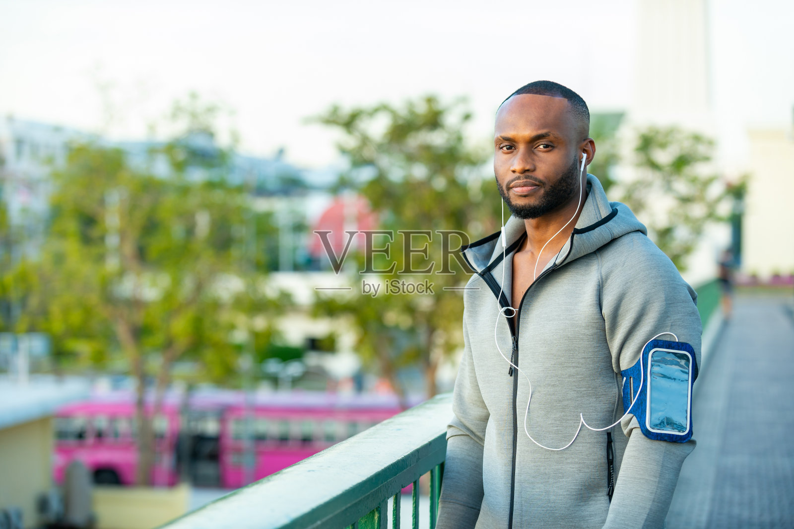 非洲男子运动员穿着运动服，一边在城市里慢跑，一边听着耳机和智能手机里的音乐照片摄影图片