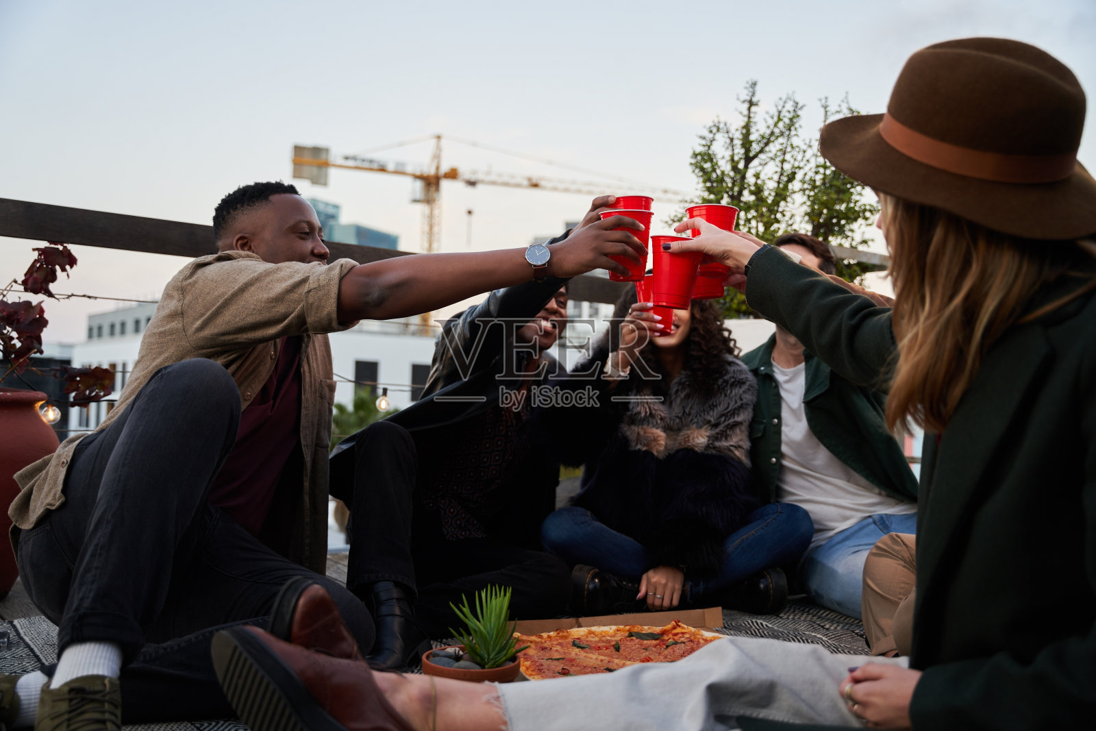 来自各地的朋友们在城市的屋顶露台上用红色的杯子举杯祝酒，享受美好时光照片摄影图片