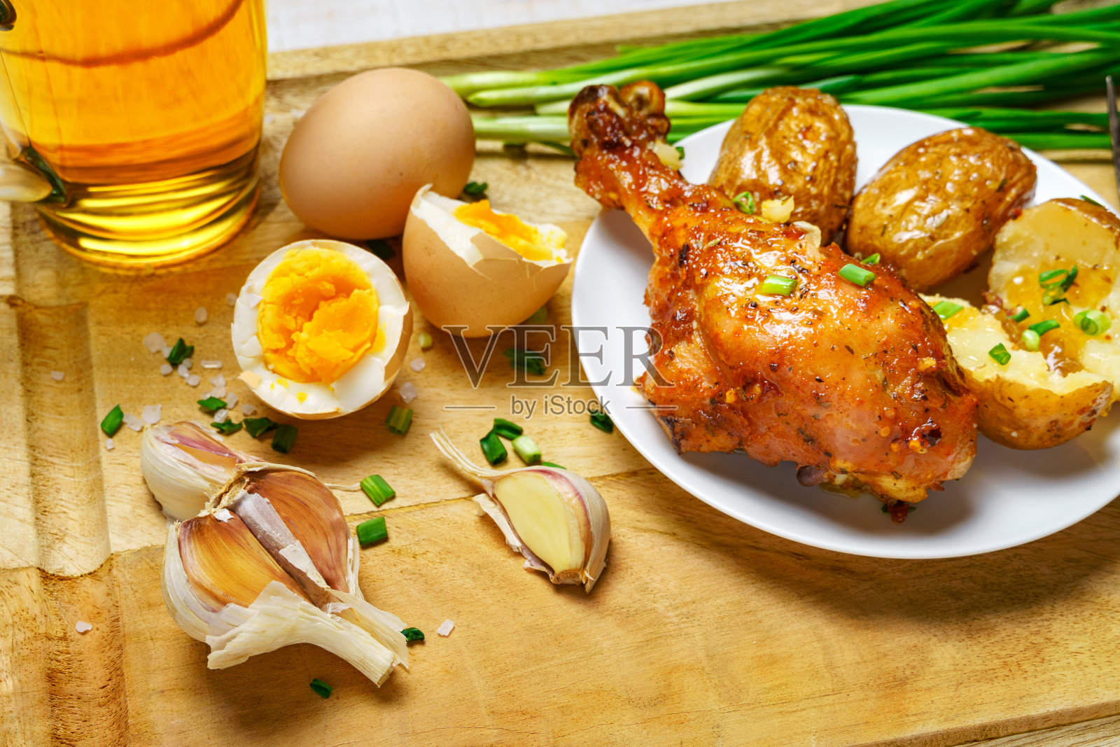 乡村风味的美味午餐，健康的食物——一杯啤酒，炸鸡和未剥皮的土豆，鸡蛋，青葱，盐和大蒜，煮熟的食物放在白色木板上照片摄影图片