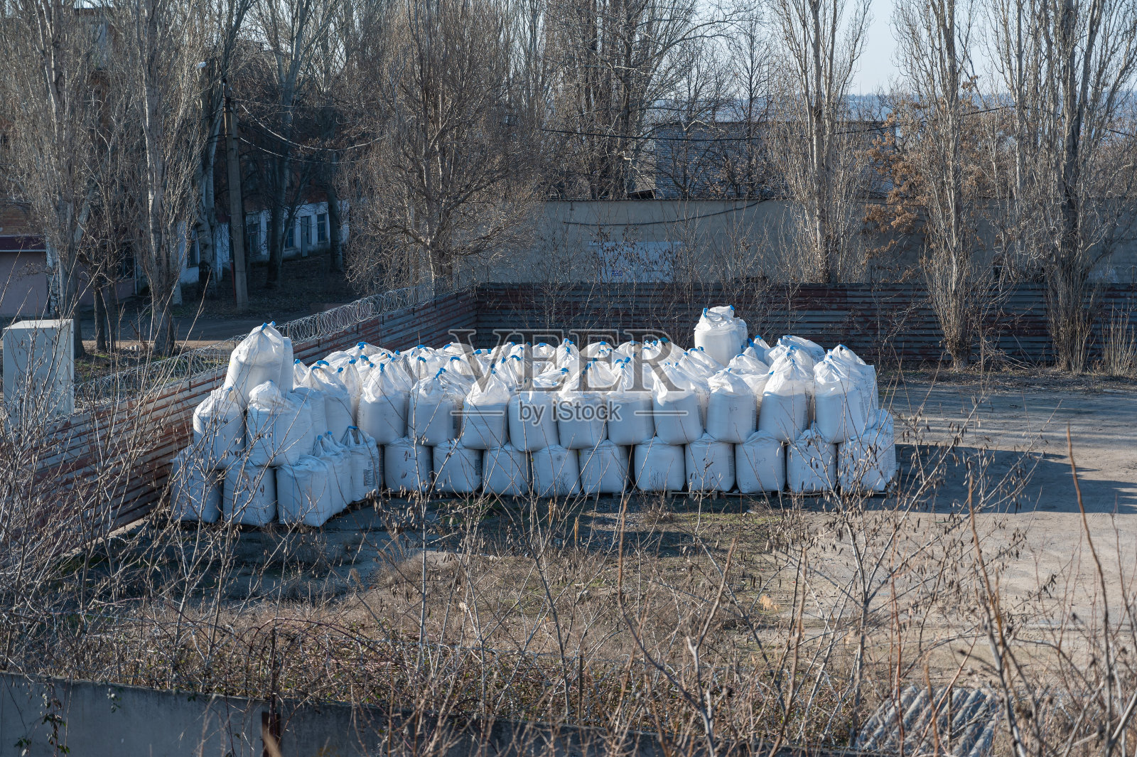 一堆大袋子在户外。工业仓库。仓库周围都是没有叶子的树。照片摄影图片