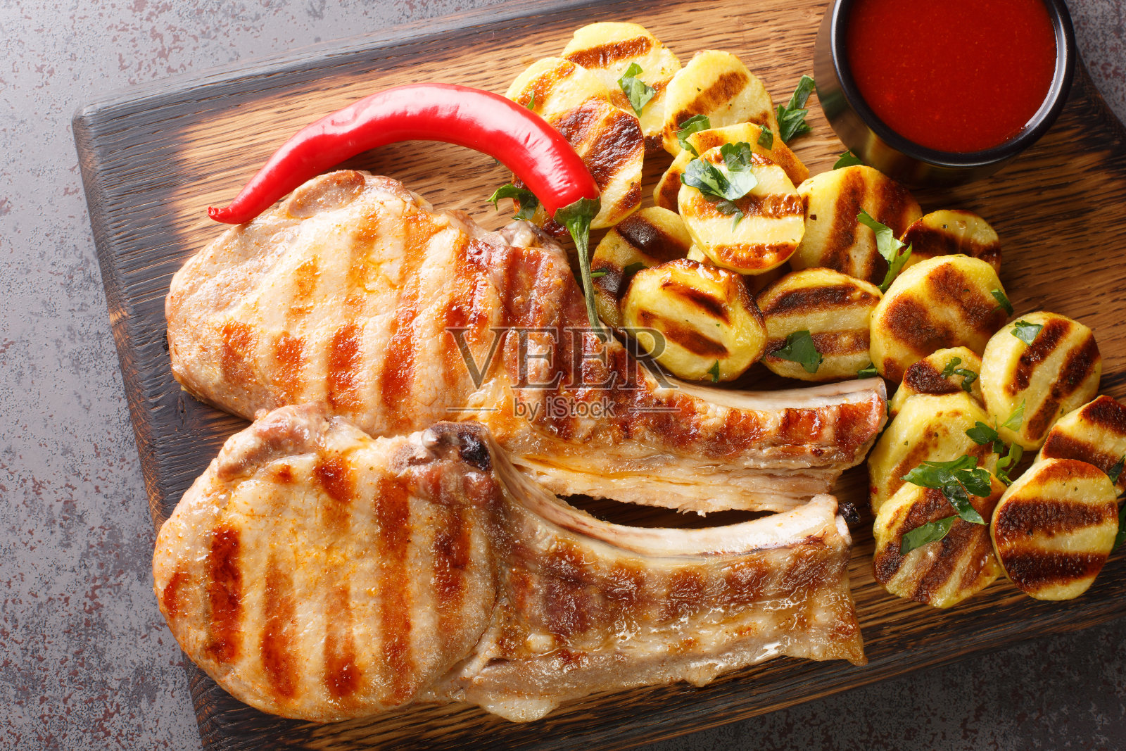 烤猪肉牛排上的骨头与调味料和烤土豆在木板上的特写。水平的俯视图照片摄影图片