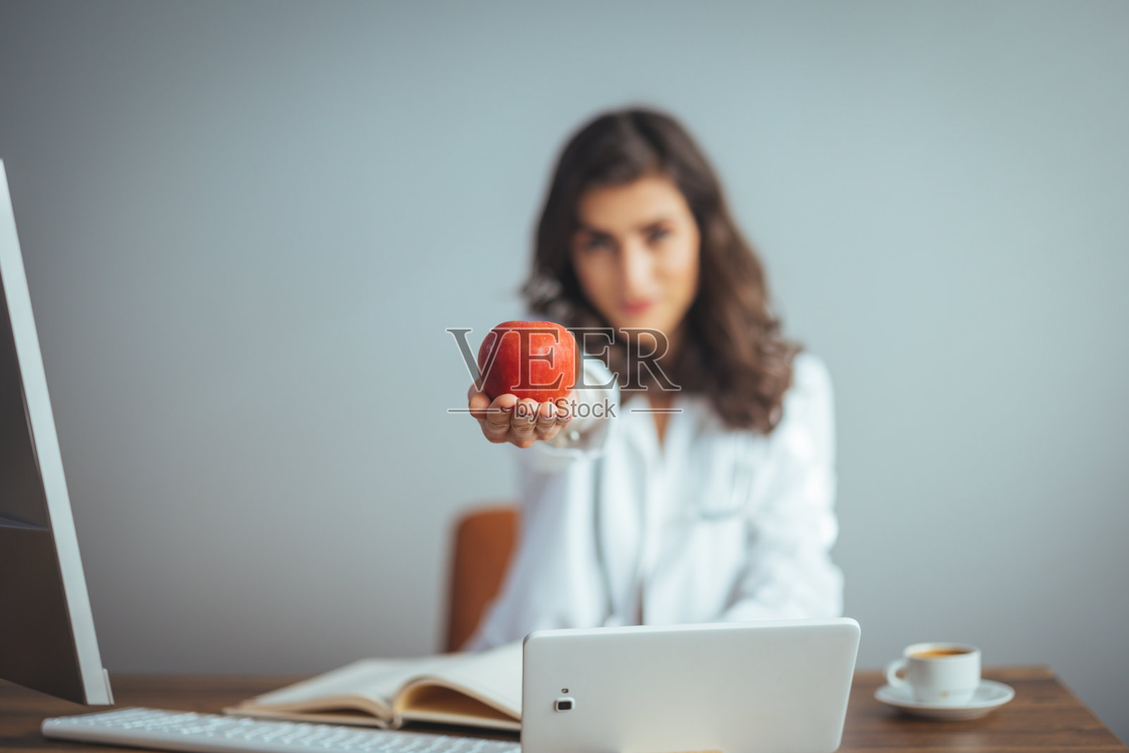 漂亮的女医生，穿着白大褂，面带微笑，手里拿着一个苹果。照片摄影图片