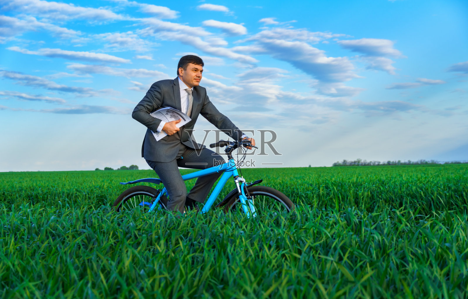 商人穿着西装，骑着一辆带着报告或文件的自行车穿过绿油油的草地，春天的自然美景，经营理念照片摄影图片