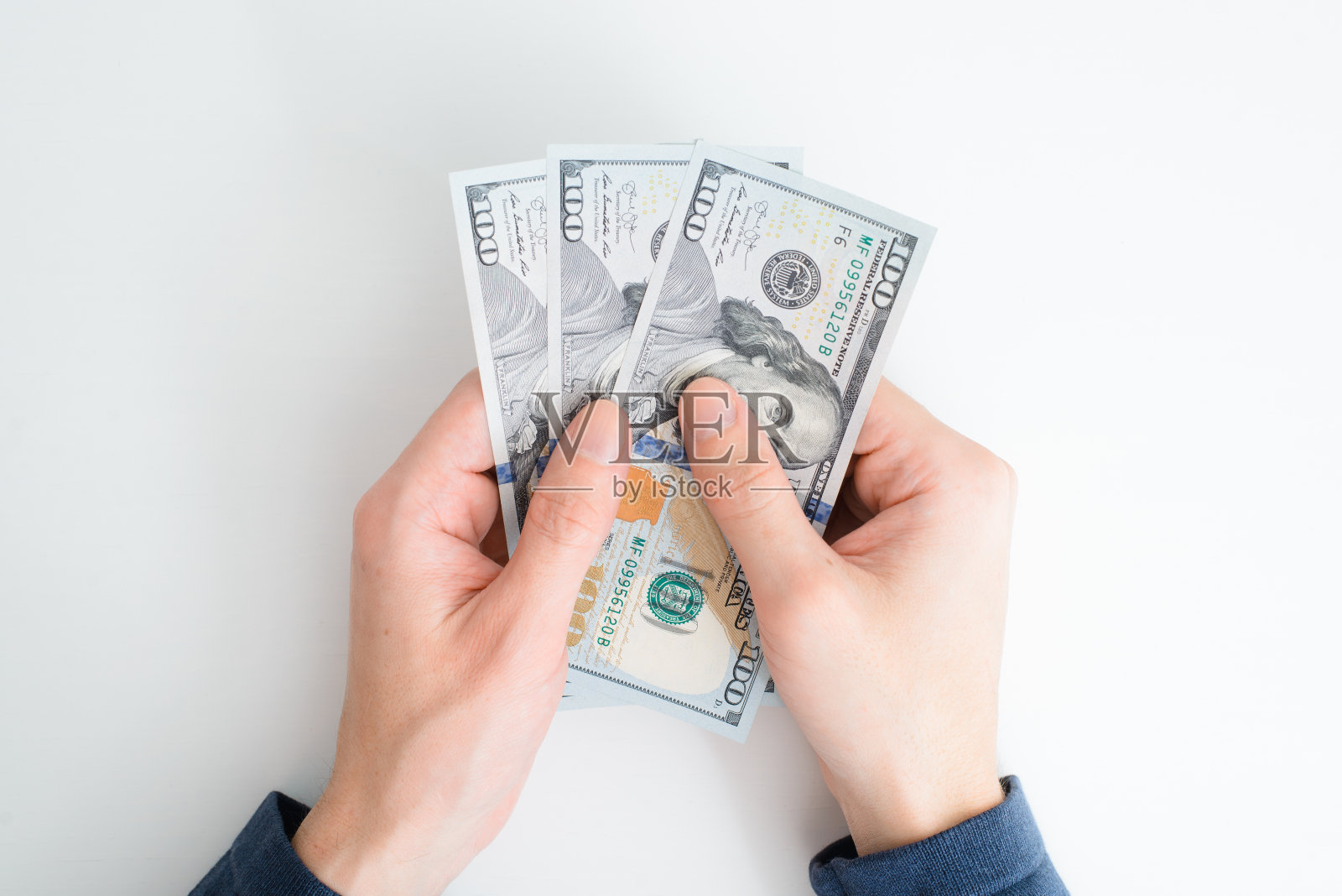 俯视图手数钱。人类白种人手握百元大钞，白色背景上的现金，特写镜头照片摄影图片