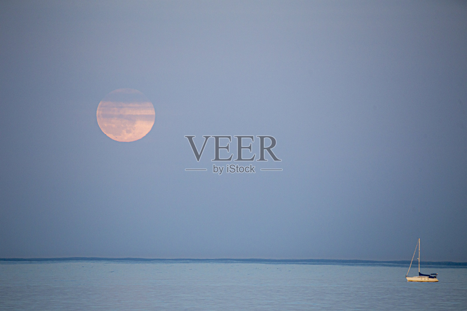 水面上升起一轮满月，前景是一艘小帆船。日落时月亮升起的帆船。月亮在海面升起，游艇漂浮在水面上。Denia西班牙阿利坎特照片摄影图片