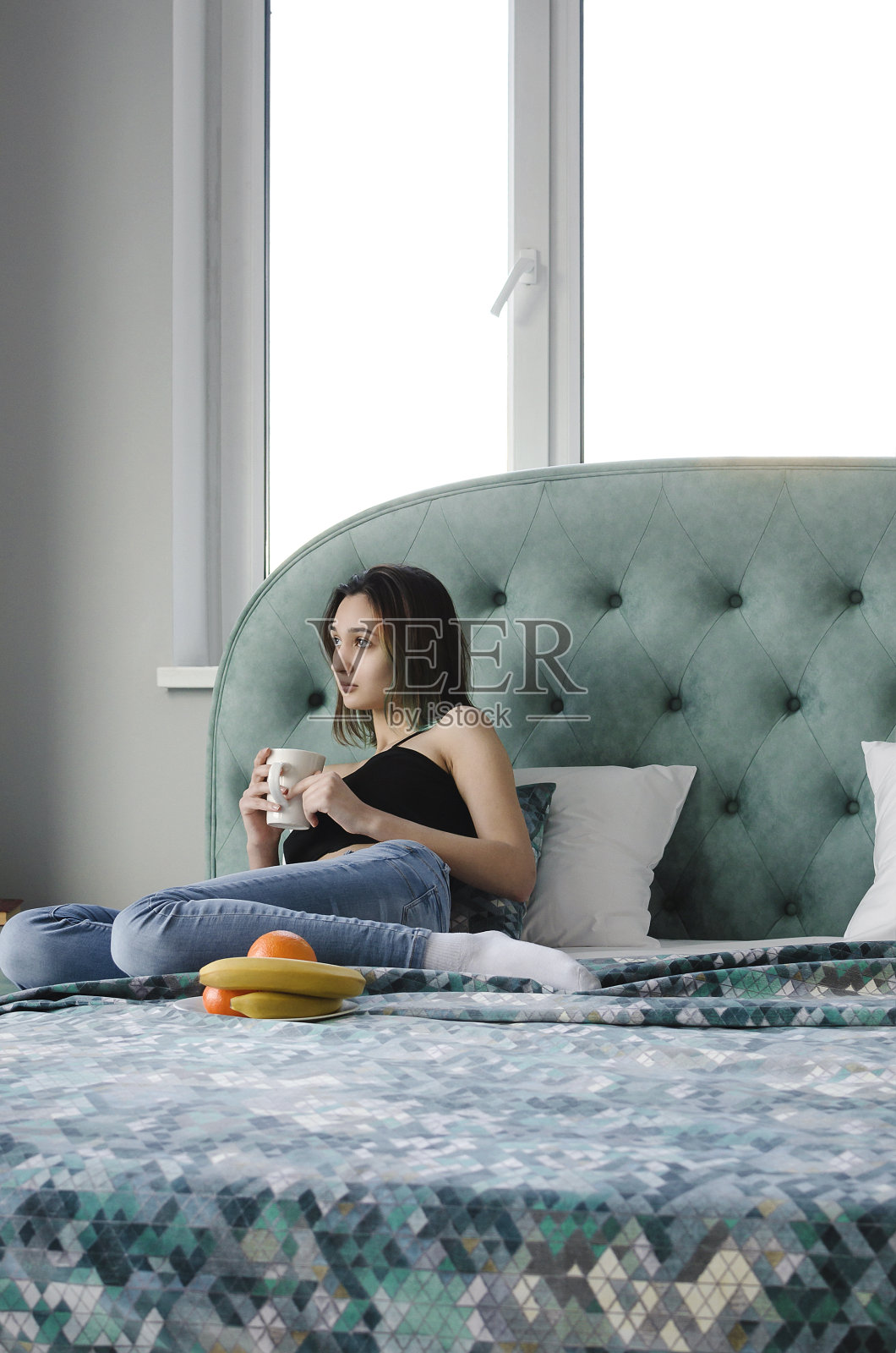 一个漂亮的女孩在一张漂亮的现代床上吃早餐和喝茶。生活理念，垂直摄影。照片摄影图片