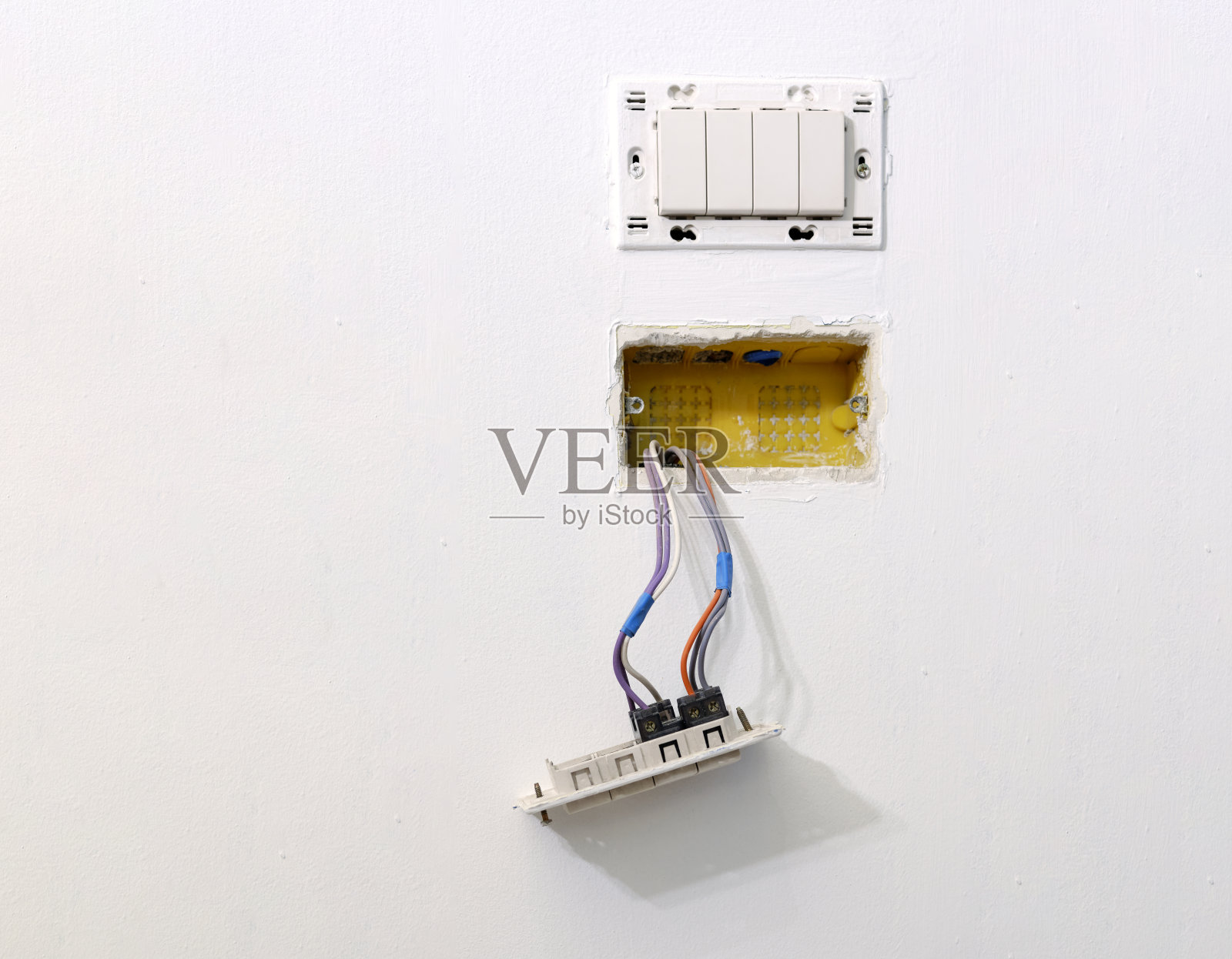 在一间正在装修的公寓里，彩色电缆从白色的墙壁上从电箱的波纹管中伸出来。按钮和开关壁挂式电箱。照片摄影图片